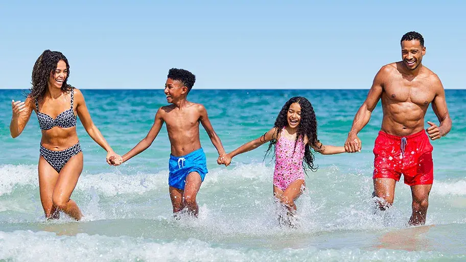 A cheerful family dashing through the ocean surf, with their children happily splashing and playing in the water.