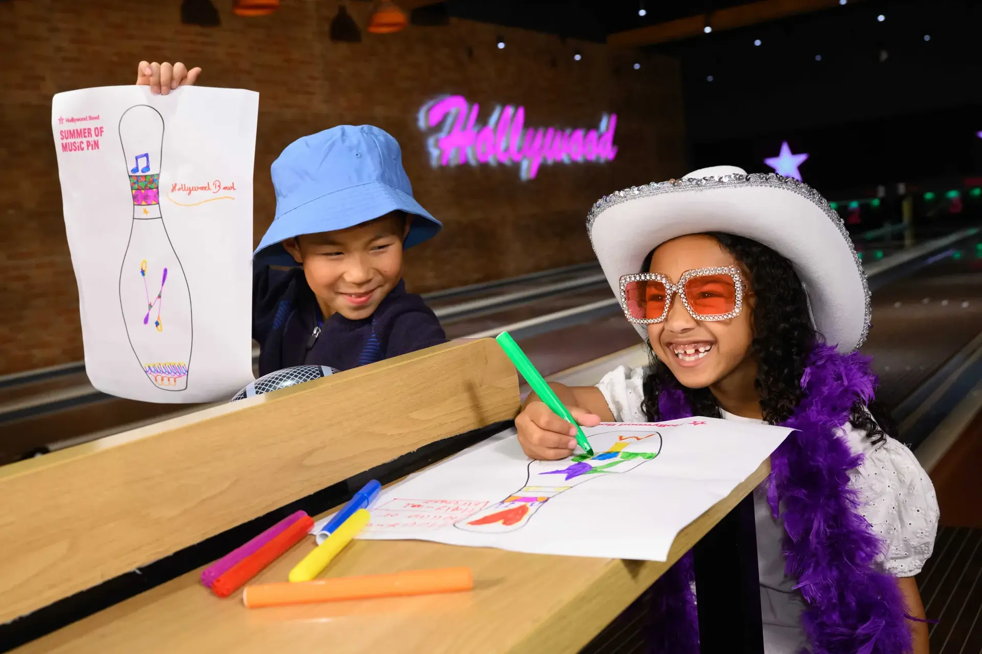 Two children are drawing on a bowling pin template, surrounded by colourful designs and playful expressions.