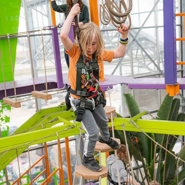 A child joyfully climbing a thick rope, reaching for the top with determination and excitement.