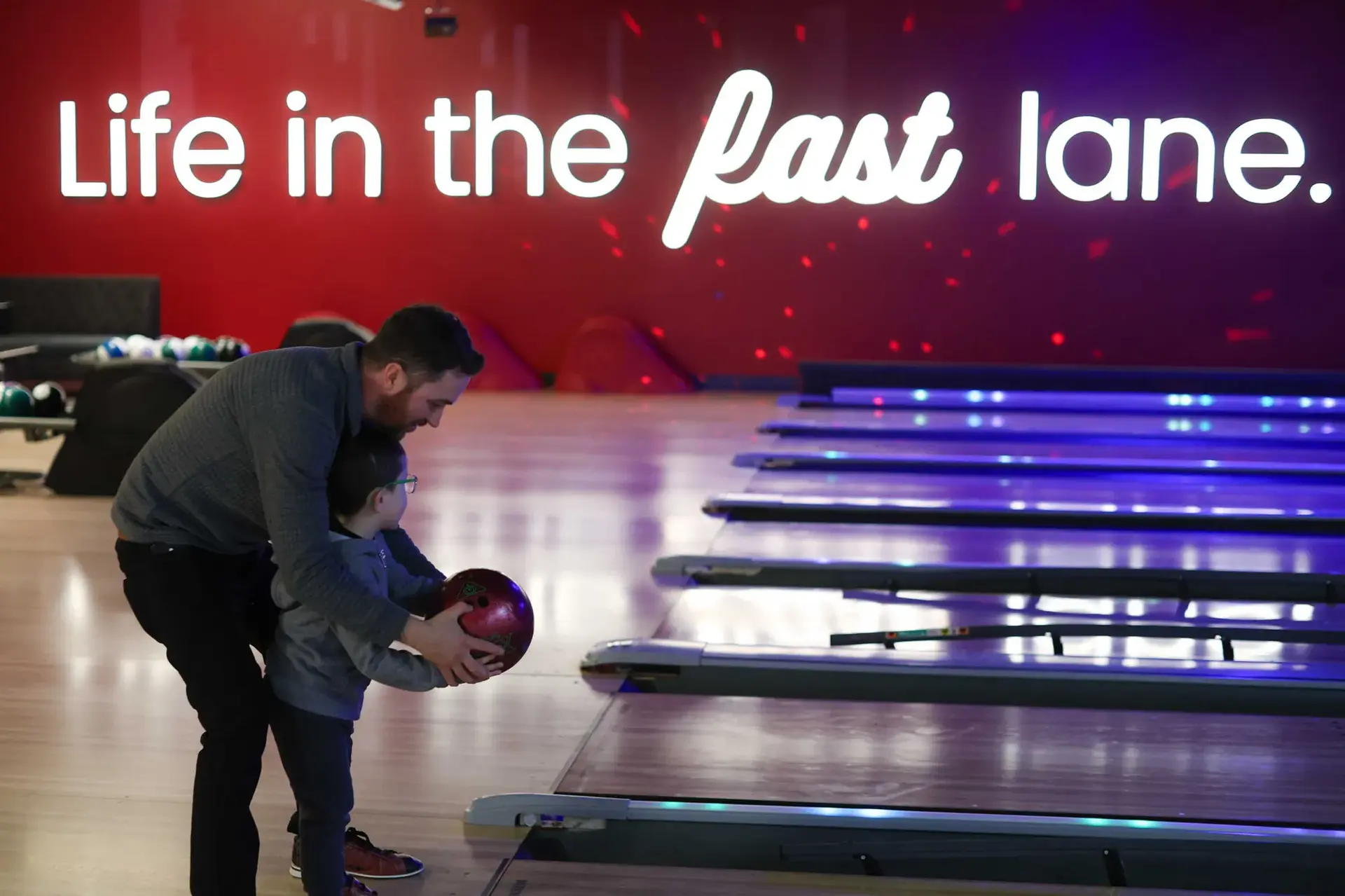 A man and a child are having fun bowling in a vibrant bowling alley, surrounded by bright lights and laughter.