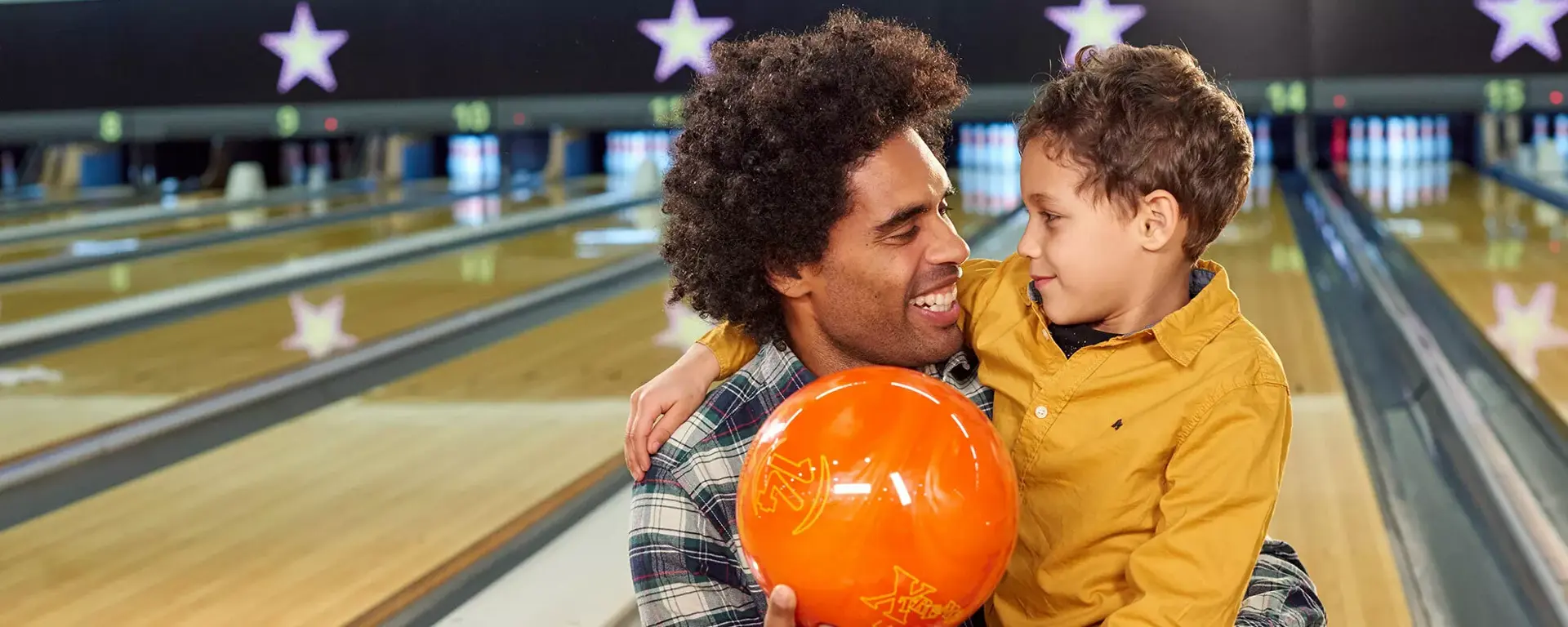 Young boy and dad smiling with a bowling ball on lanes