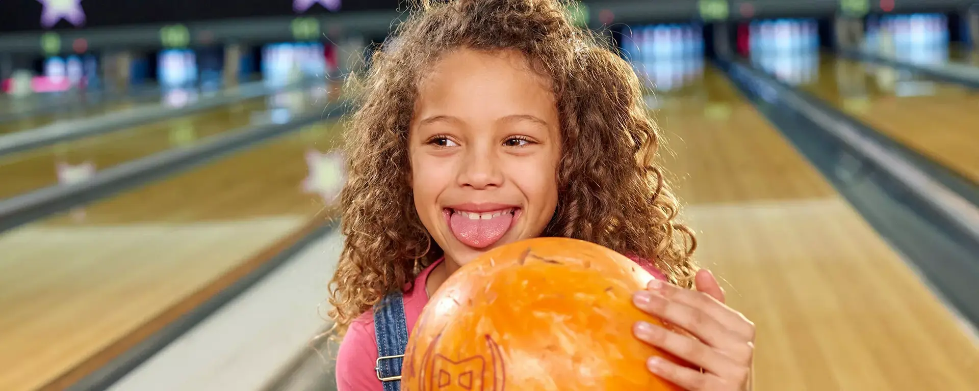 Young girl holding bowling ball pulling a silly face