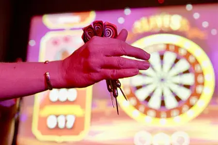 A person holds a dart in front of a dartboard, preparing to throw it at the target.