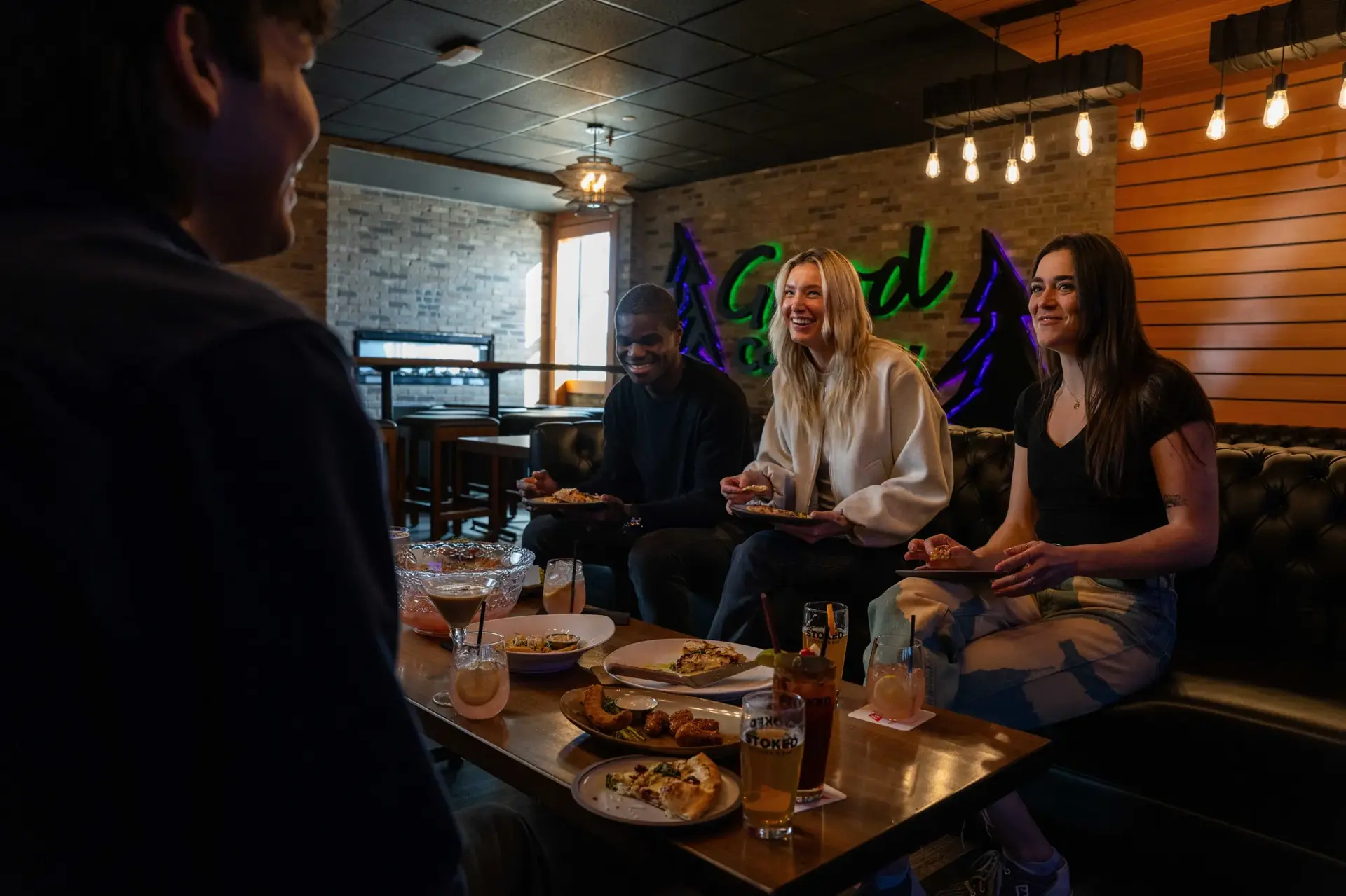 Three young adults gathered around a table, enjoying a meal and drinks, creating a warm and friendly atmosphere at Stoked by Splitsville Bowl