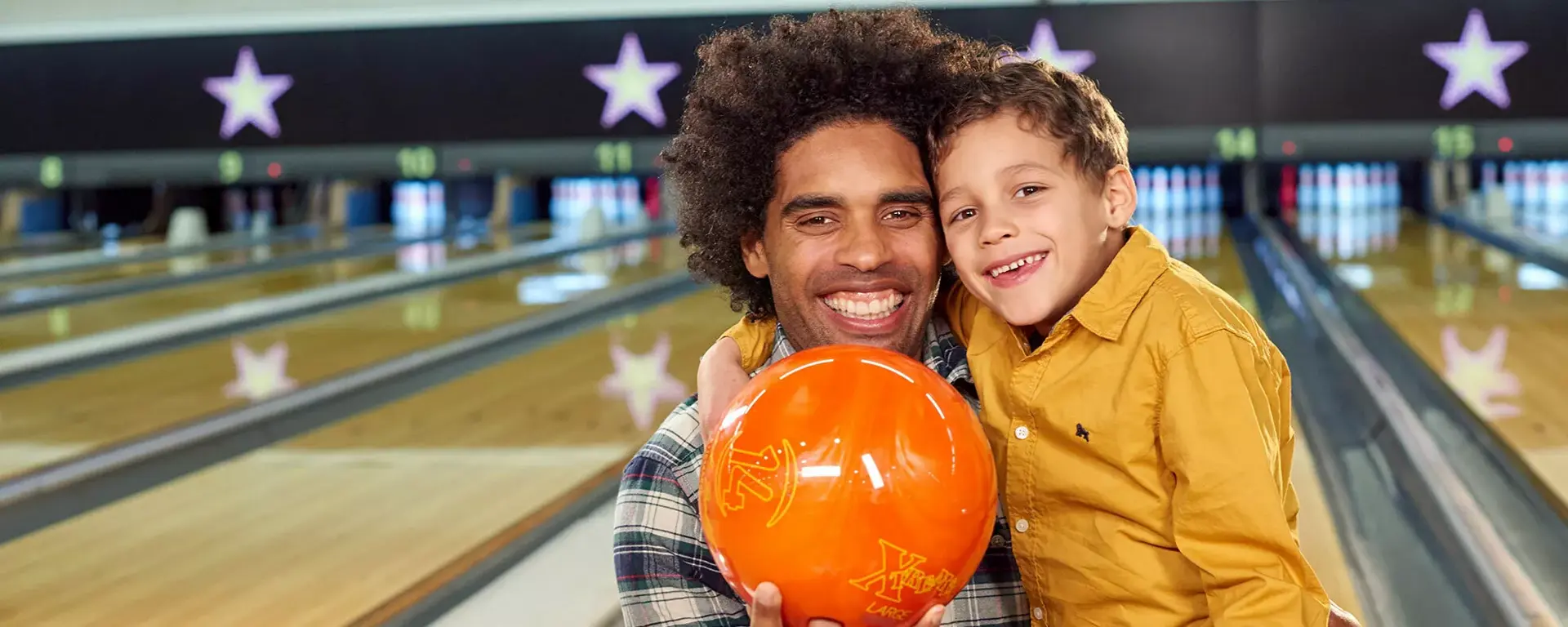 Young boy and dad holding bowling ball on lanes