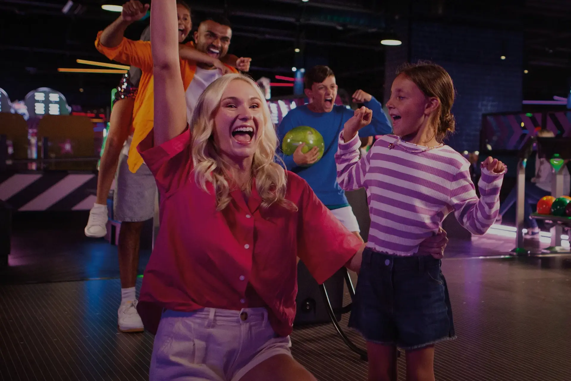 A family playing bowling together, with one person in the act of rolling a bowling ball down the lane.
