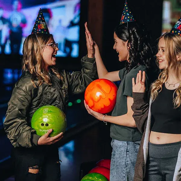 A group of girls at a bowling alley cheerfully raising their hands in excitement.