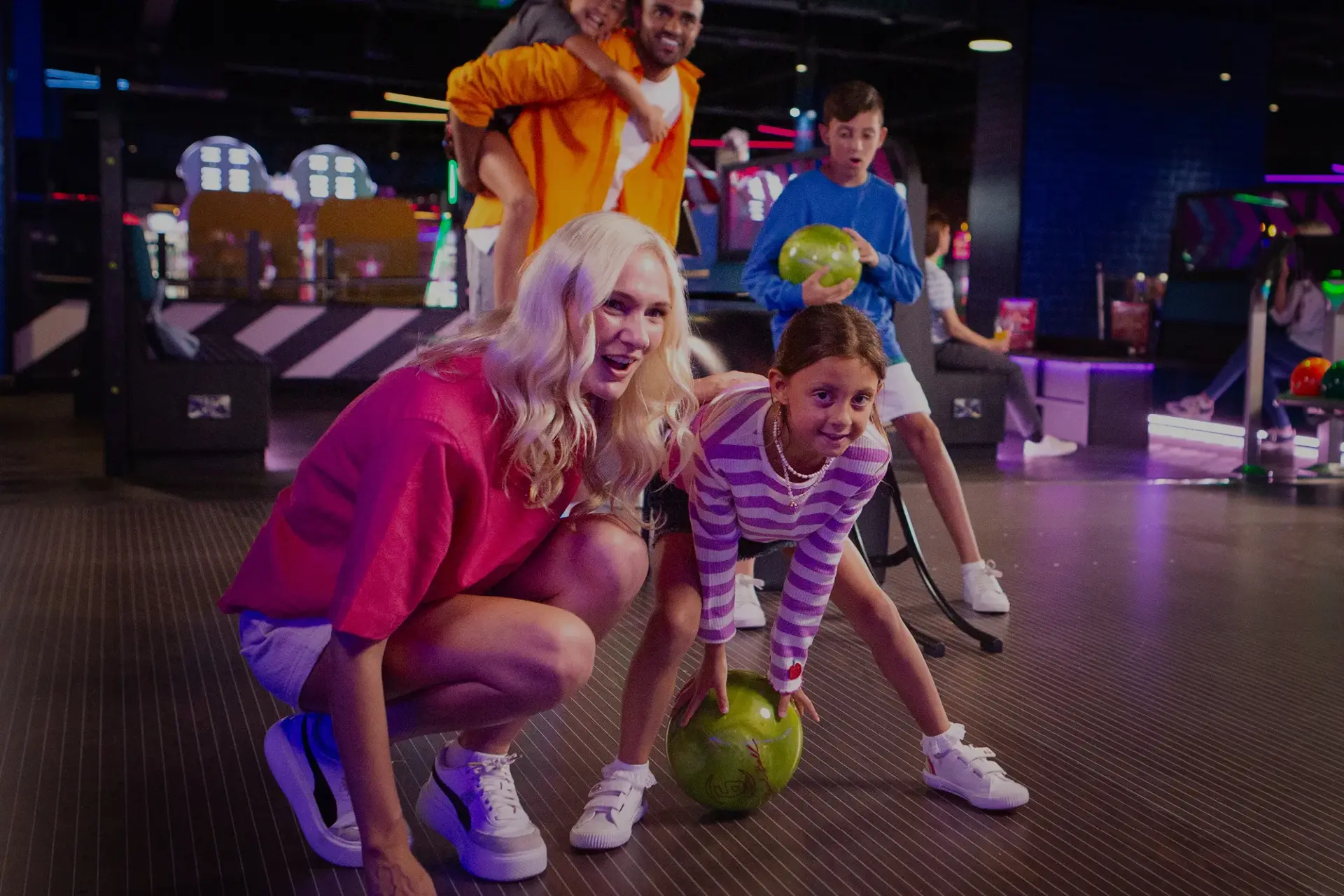 A family playing bowling together, with one person in the act of rolling a bowling ball down the lane.