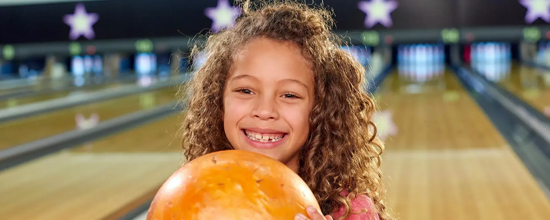 Young girl holding bowling ball on lanes