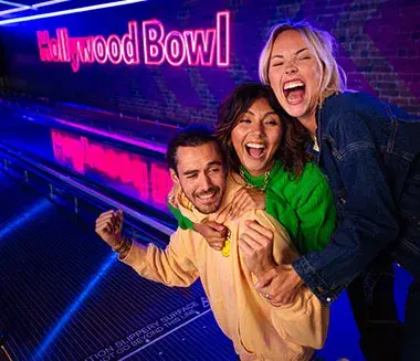 A couple smiles while holding a bowling ball and enjoying drinks at Hollywood Bowl