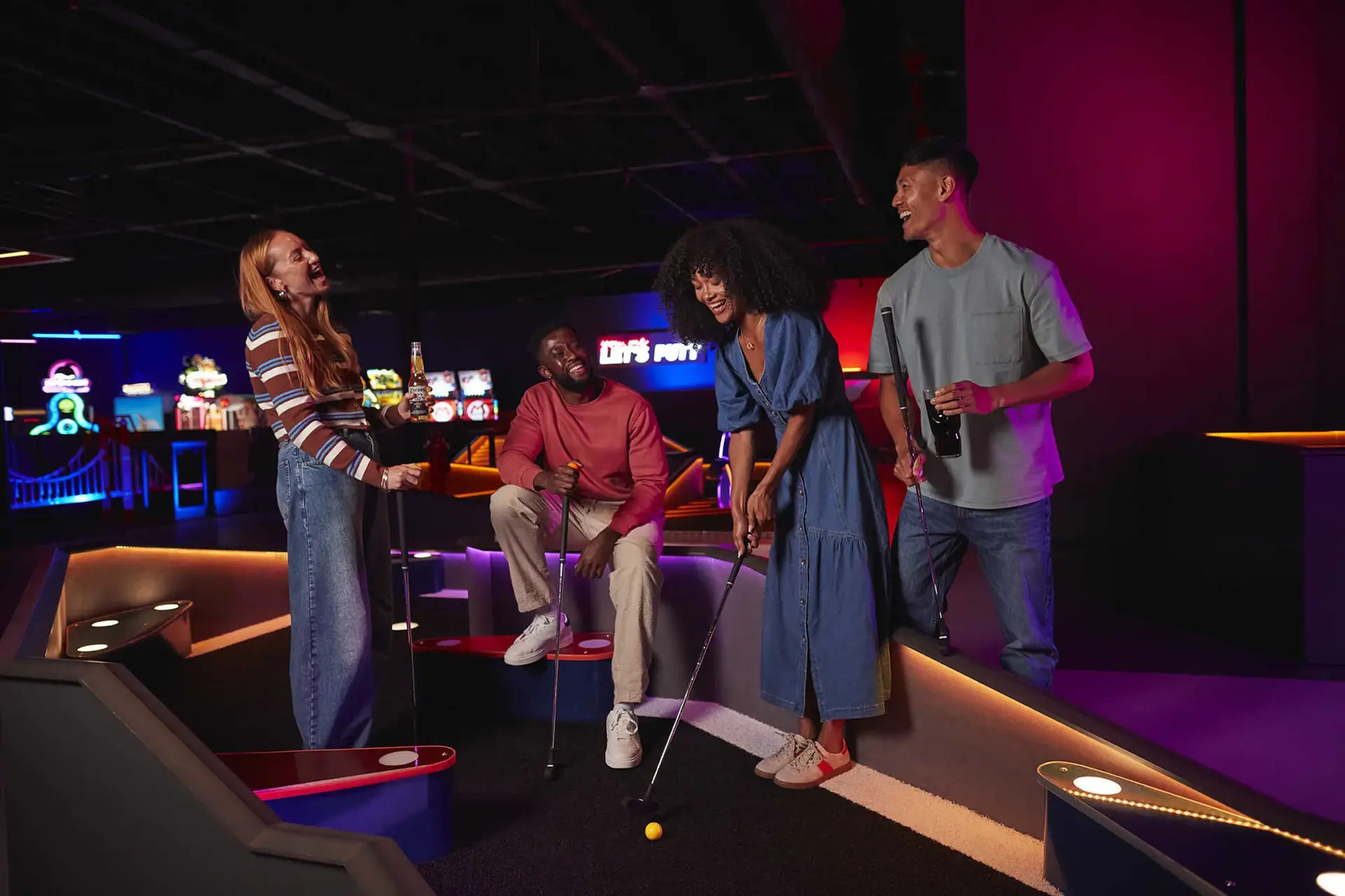 People laughing and playing mini golf together at Putt and Play, surrounded by playful decor and bright lights.