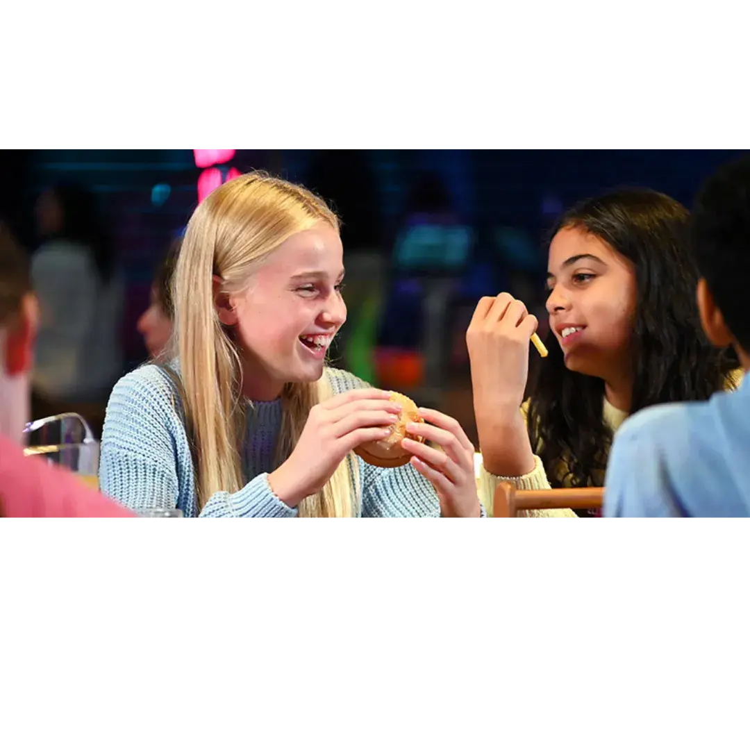 Two girls enjoying burgers together at a restaurant, smiling and engaged in conversation