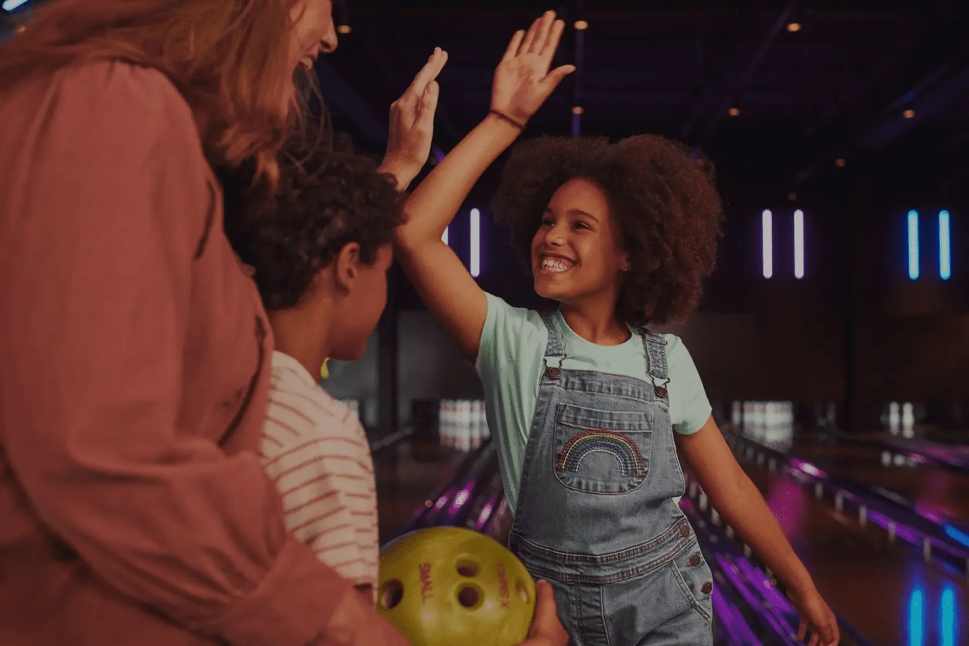 A woman and two children joyfully bowling together at a lively bowling alley, sharing smiles and laughter.