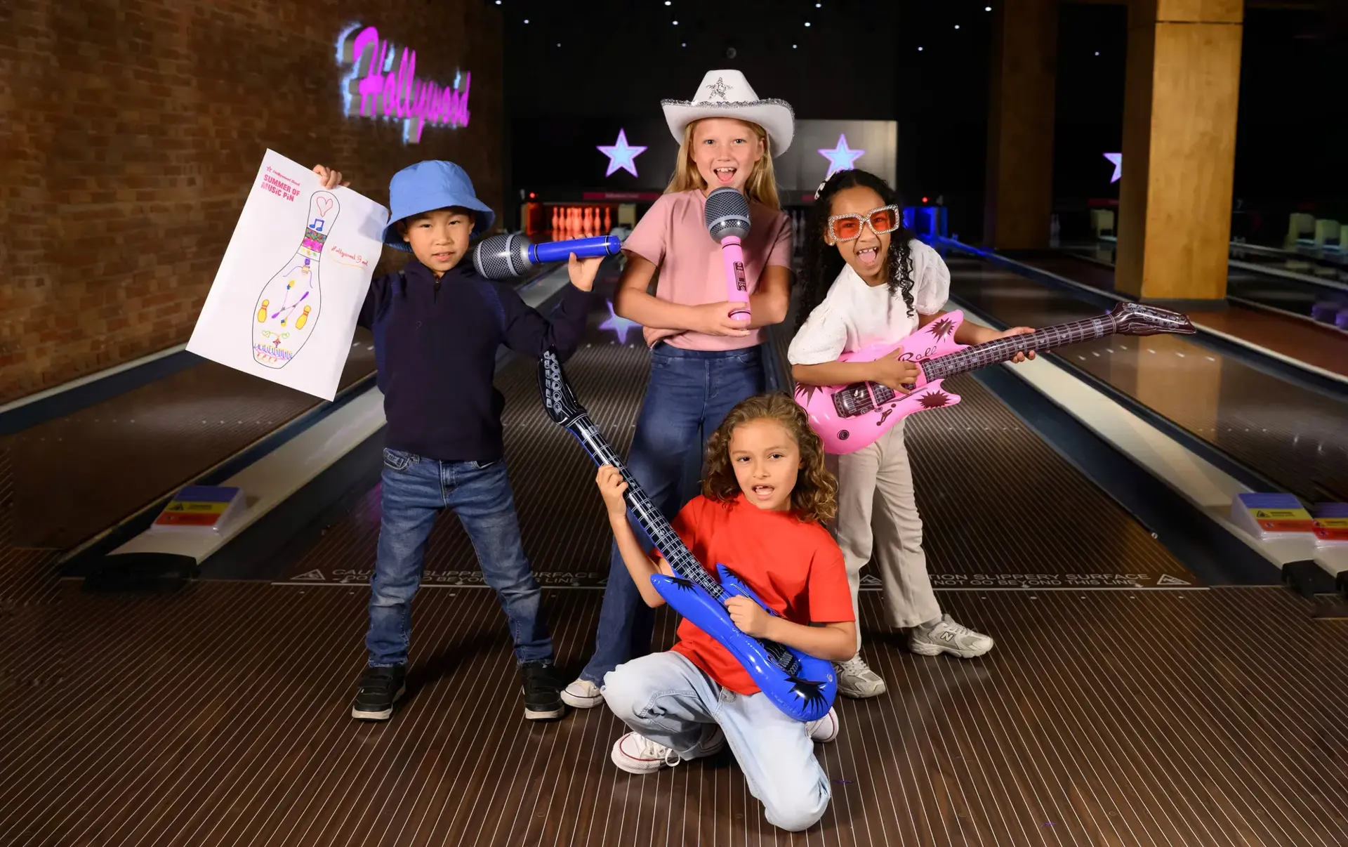 Four kids pose with guitars, surrounded by bowling pins, showcasing a fun and lively atmosphere.
