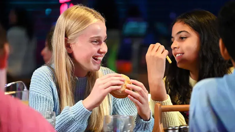 Two girls enjoying burgers together at a restaurant, smiling and engaged in conversation