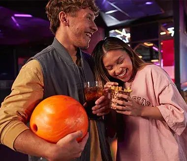 A couple smiles while holding a bowling ball and enjoying drinks at Hollywood Bowl